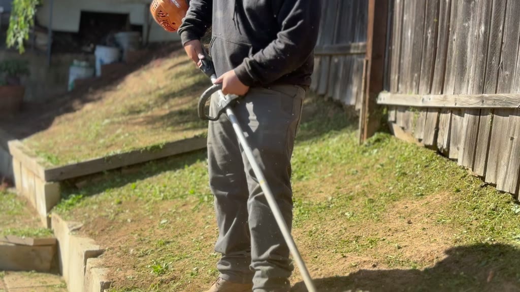 Ledezma Landscaping crew member using a weed whacker along a wooden fence